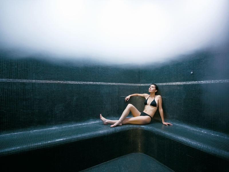 Femme en bikini se détend dans un sauna spa sombre et moderne avec un éclairage tamisé.