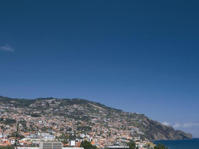 Vue sur une ville côtière avec des montagnes en arrière-plan et un ciel bleu clair au-dessus de la mer.