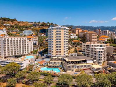 Stadtansicht mit mehrstöckigen Gebäuden, Hotels, Pool und Bergen im Hintergrund bei blauem Himmel.