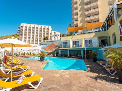 Moderner Hotelpool mit blauer Wasserfläche, gelben Sonnenliegen und Sonnenschirmen bei klarem Himmel.
