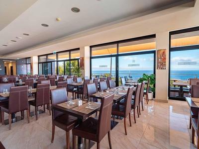 Helles Restaurant mit vielen Holztischen, Stühlen und großen Fenstern mit Meerblick.