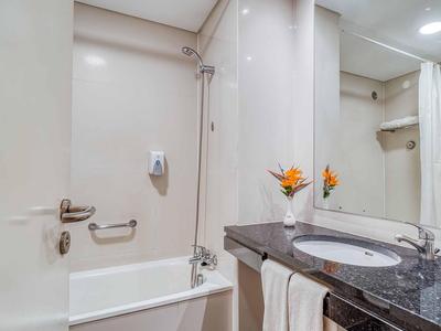 Weißes Badezimmer mit Badewanne, Spiegel, dunkler Arbeitsplatte und orangefarbenen Blumen.