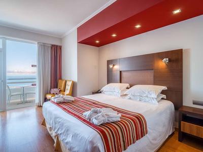 Modernes Hotelzimmer mit großem Bett, Holzfront, roten Akzenten und Balkon mit Meerblick.