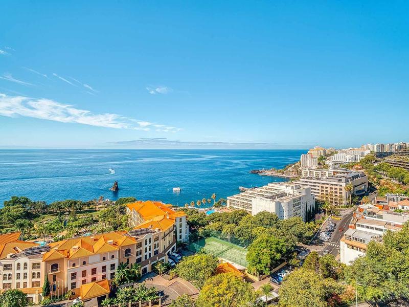 Blick auf eine Küstenstadt mit orangen Dächern, grünen Bäumen und blauem Himmel und Meer.