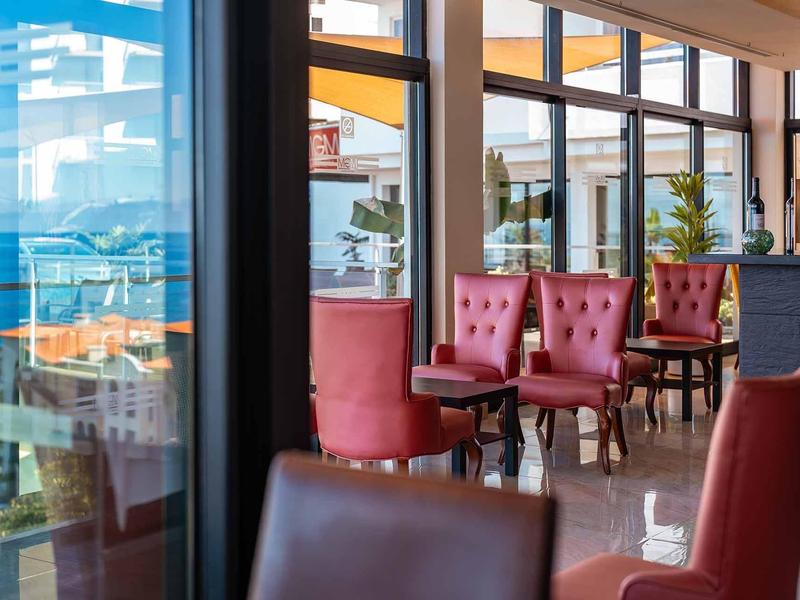 Moderner Innenraum mit roten, gepolsterten Stühlen und großen Fenstern mit Blick nach draußen.