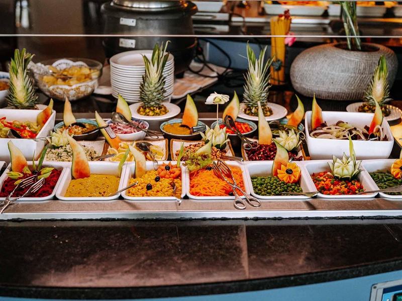 Buffet mit verschiedenen bunten Speisen, darunter Obst, Gemüse und Saucen in weißen Schalen.