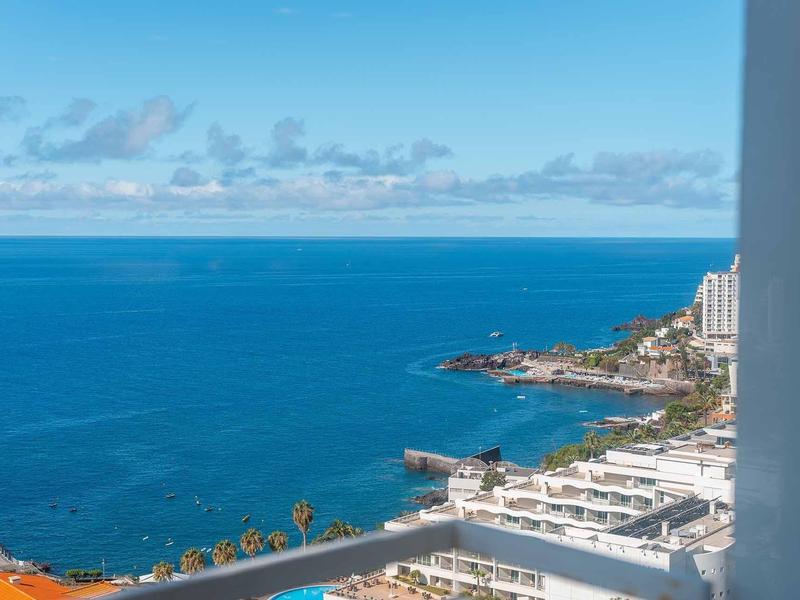 Blick auf ruhiges blaues Meer und Küste mit Gebäuden unter blauem Himmel mit wenigen Wolken.