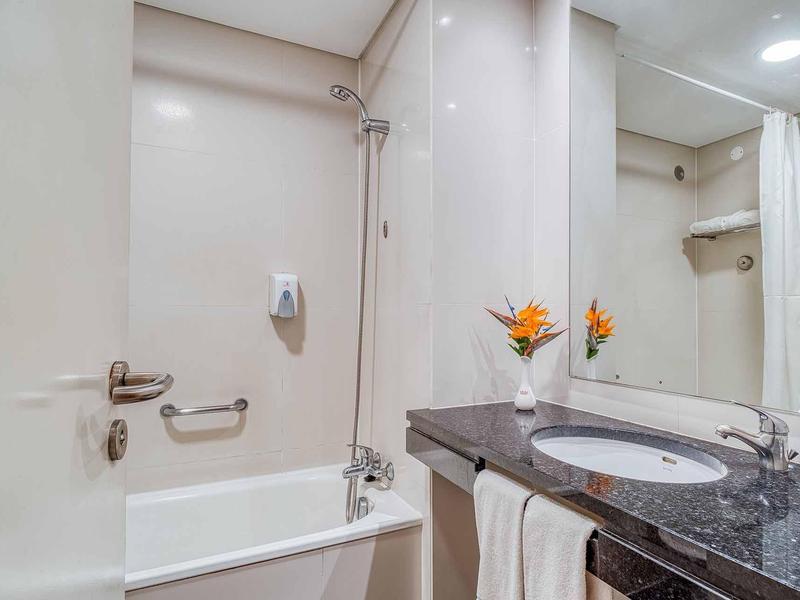 Weißes Badezimmer mit Badewanne, Spiegel, dunkler Arbeitsplatte und orangefarbenen Blumen.