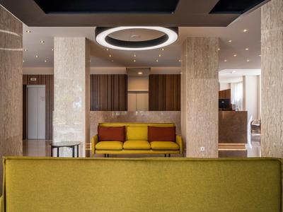 Moderner Wohnraum mit senfgelben Sofas, Holzpaneelen und rundem Deckenlicht im Zentrum.