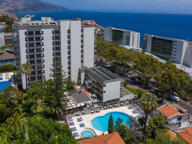 Moderne weiße Hochhäuser mit Pool, Palmen und Blick aufs blaue Meer im sonnigen Küstengebiet.