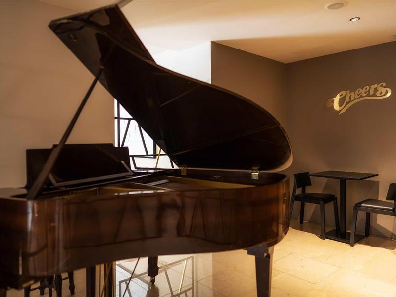 Großer brauner Flügelklavier in hellem Raum mit runder Ecke und dunklen Hockern.