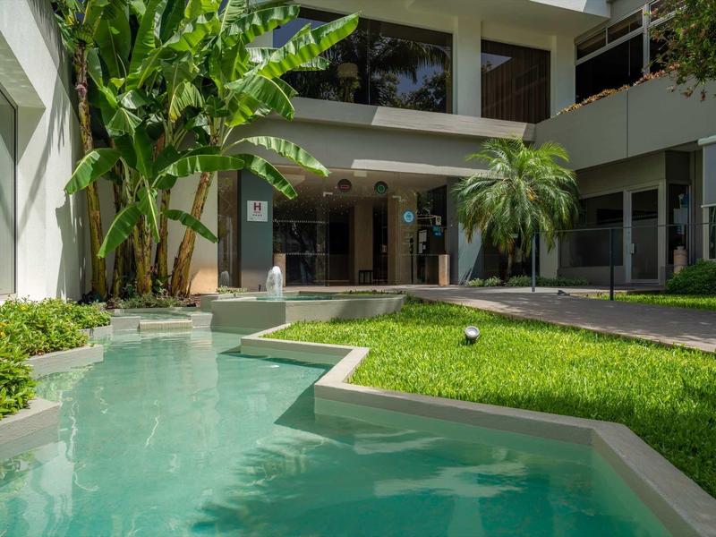 Modernes Gebäude mit Schwimmbecken, grünen Pflanzen und Rasen im Vordergrund.