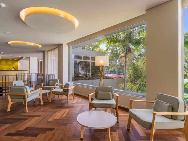 Moderner Wohnbereich mit großen Fenstern, Holzboden, gemütlichen Sesseln und warmem Deckenlicht.