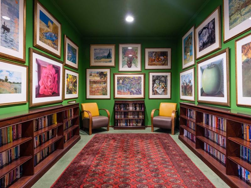 Kleiner grüner Leseraum mit Bücherregalen, gemütlichen Stühlen und zahlreichen gerahmten Bildern.