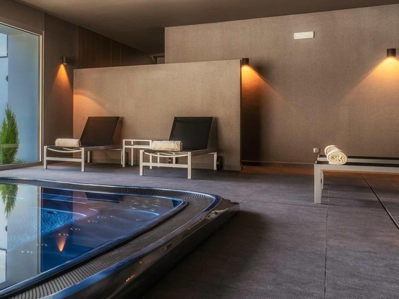 Moderner Wellnessbereich mit dunklem Pool, zwei Liegestühlen und warmem Wandlicht.
