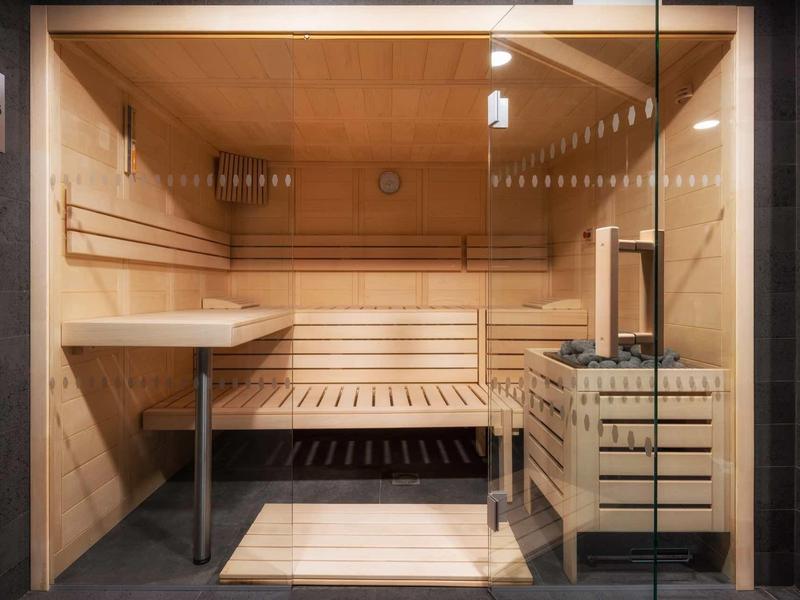 Moderne Holzsauna mit Glasfront, Holzbänken, Ofen und kleinem Holztisch im Inneren.