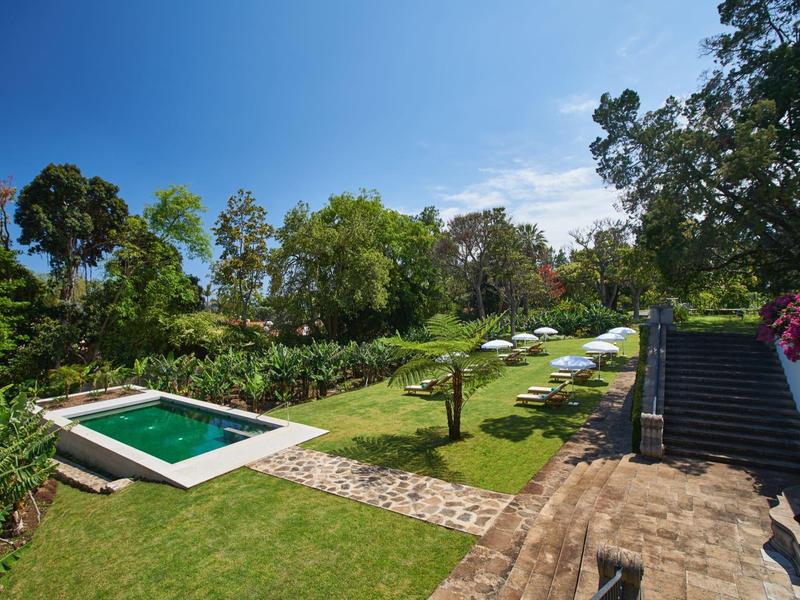 Giardino verde con piscina, ombrelloni bianchi e cielo azzurro.
