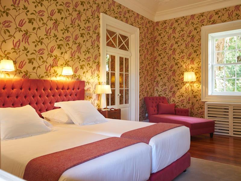 Elegante camera d'hotel con due letti singoli, carta da parati floreale e divano rosso.