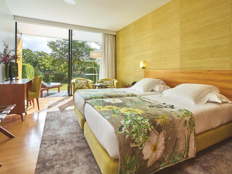 Camera d'hotel luminosa con due letti, pareti in legno e vista sul giardino.