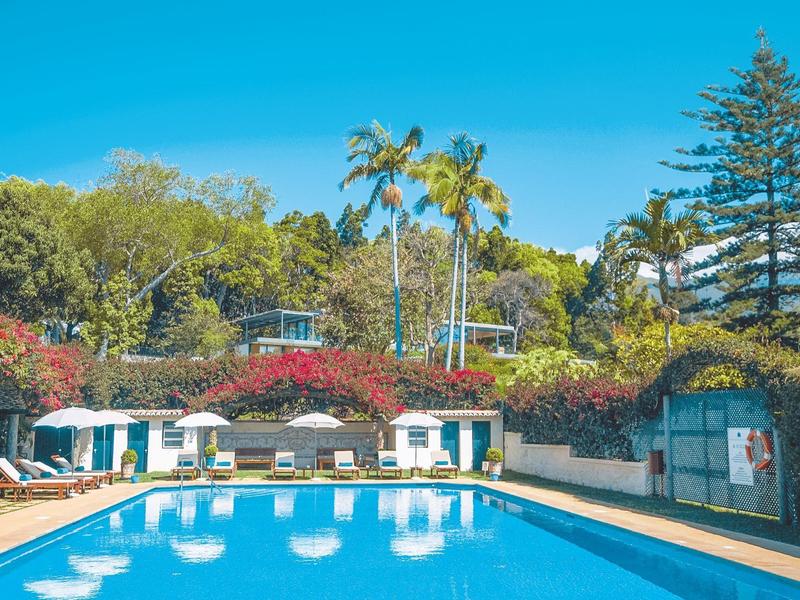 Grande piscina davanti a un hotel circondato da alberi sotto un cielo azzurro.