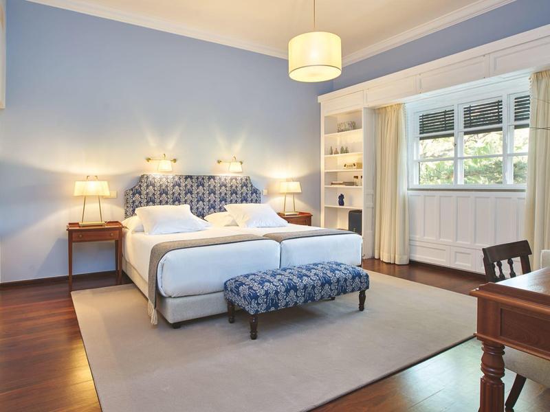 Camera d'hotel moderna con letto matrimoniale, pareti azzurro chiaro e finestra con tende.