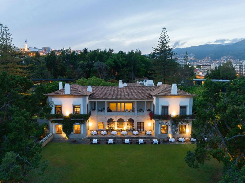 Edificio d'hotel elegante con finestre illuminate e terrazza in un ambiente verde e tranquillo.