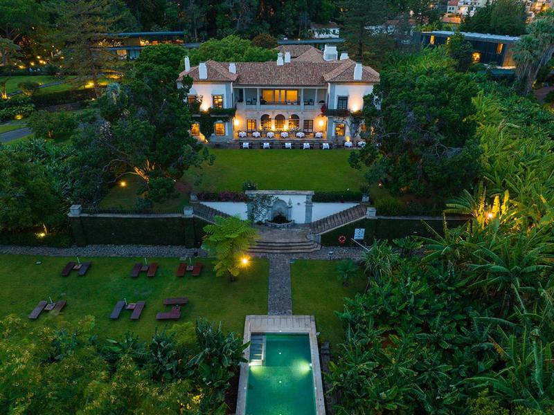 Villa elegante con piscina illuminata e giardino curato al crepuscolo.