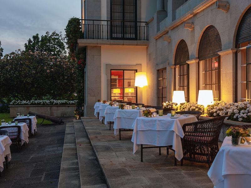 Terrazza dell'hotel di sera con tavoli apparecchiati e luce calda.