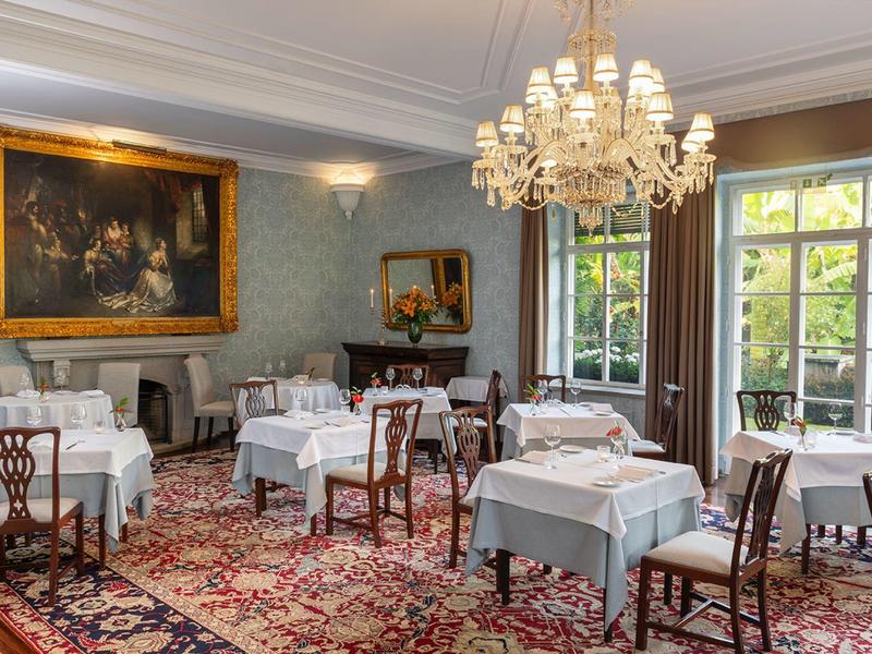 Sala da pranzo elegante con tovaglie bianche, sedie antiche e lampadario.
