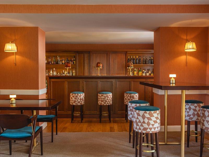 Bar accogliente dell'hotel con bancone in legno, sgabelli e luci da parete calde.