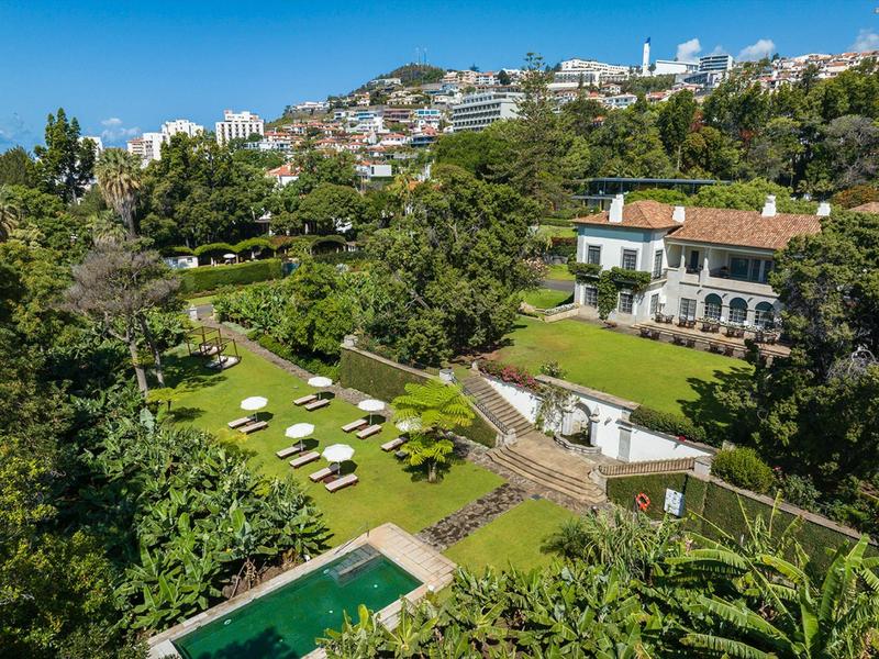 Villa di lusso con piscina e lettini in paesaggio collinare verde sotto un cielo sereno.