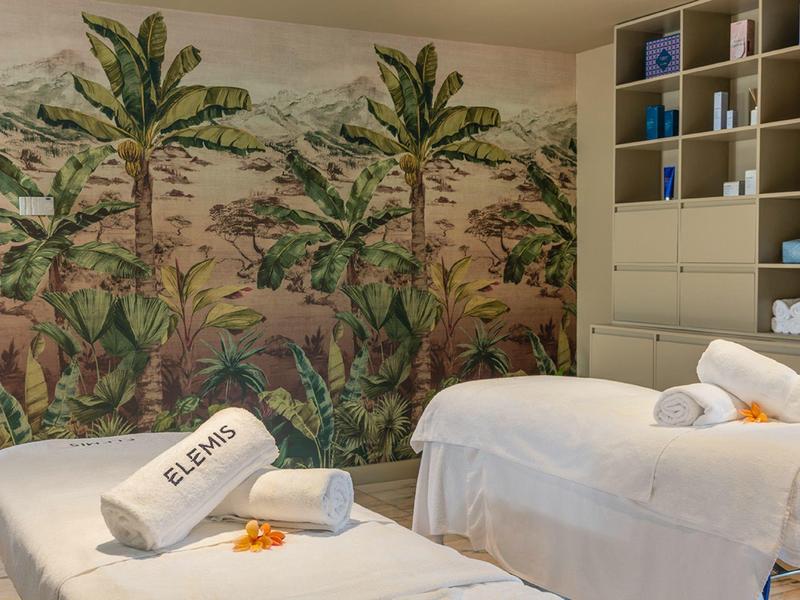 Sala relax con due lettini da massaggio davanti a un murale tropicale in una spa.