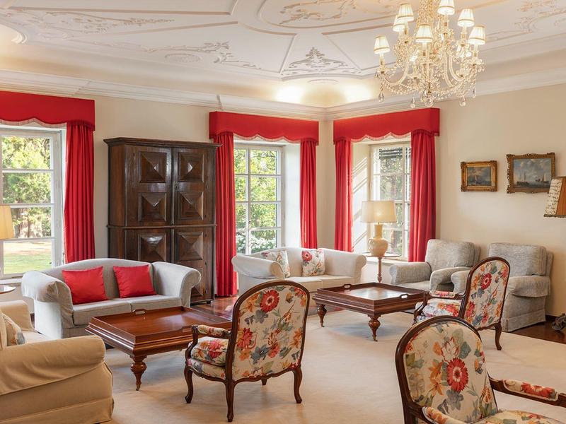 Soggiorno elegante con lampadario, tende rosse e poltrone con motivi classici.