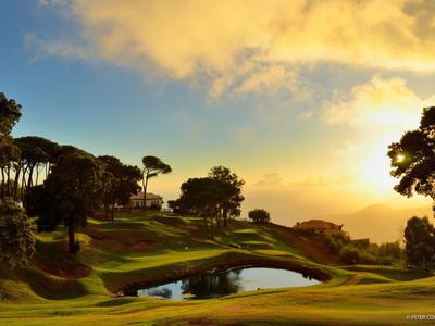 Zachód słońca nad polem golfowym z małymi stawami i drzewami.