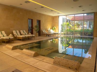 Basen kryty z leżakami i dużymi oknami z widokiem na ogród w hotelu.