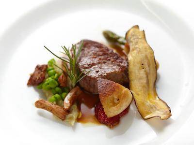 Danie gourmet z delikatnym mięsem, grzybami i warzywami podane na białym talerzu.