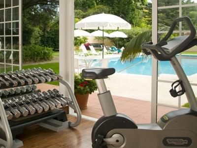 Fitnessruimte met halters en hometrainers met uitzicht op een zwembad en tuin