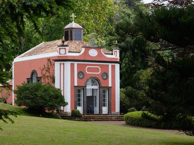 Mały czerwony budynek z białymi kolumnami i krzyżem na dachu w zielonym parku