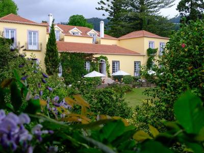 Geel landhuis met terras en tuin, omgeven door groene struiken en bomen.