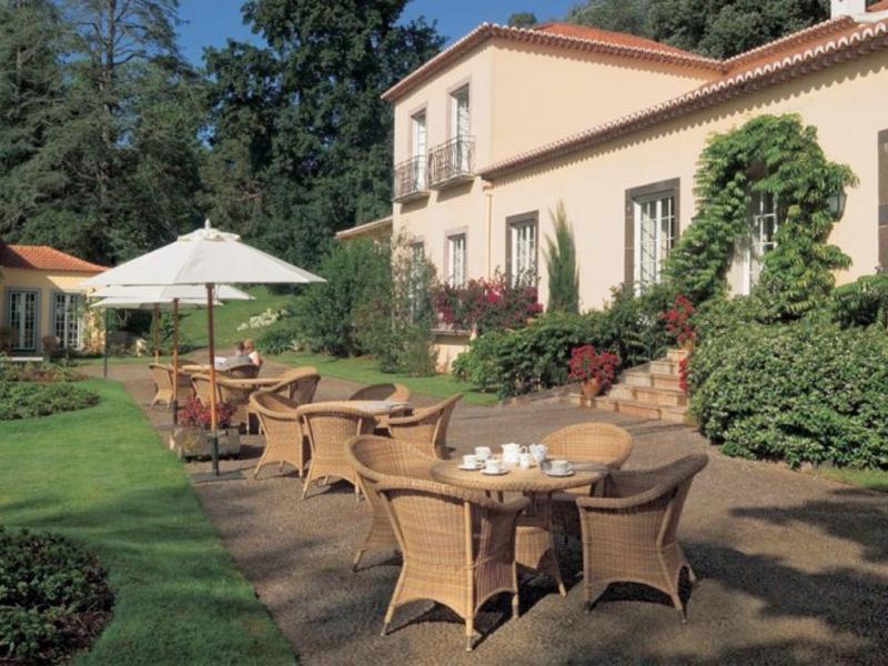 Przytulne miejsce na świeżym powietrzu z wiklinowymi krzesłami i parasolem przed jasnym, cichym budynkiem hotelu.