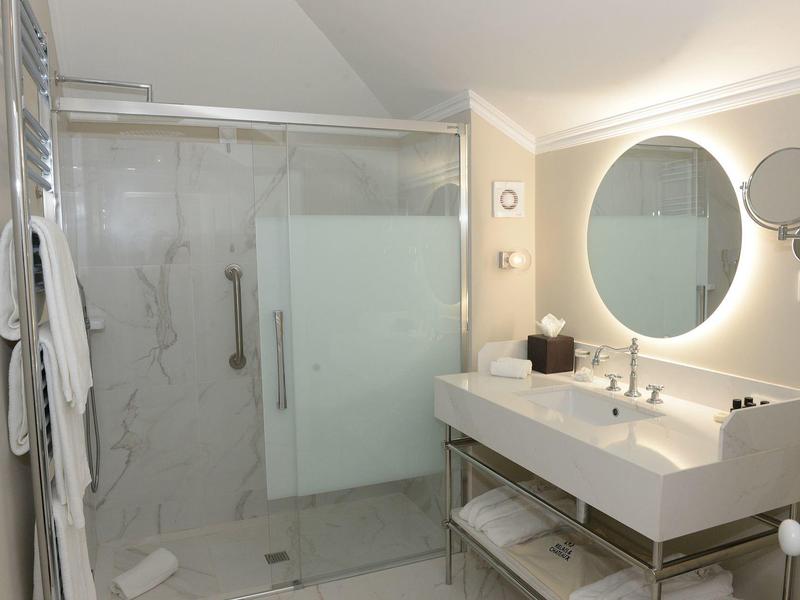 Nowoczesna łazienka z dużym prysznicem, podwójnymi umywalkami i okrągłym podświetlanym lustrem.