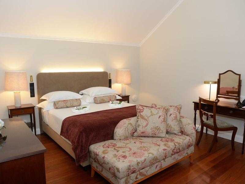 Przytulny pokój hotelowy z łóżkiem podwójnym, stolikami nocnymi, ławką i biurkiem z lustrem.