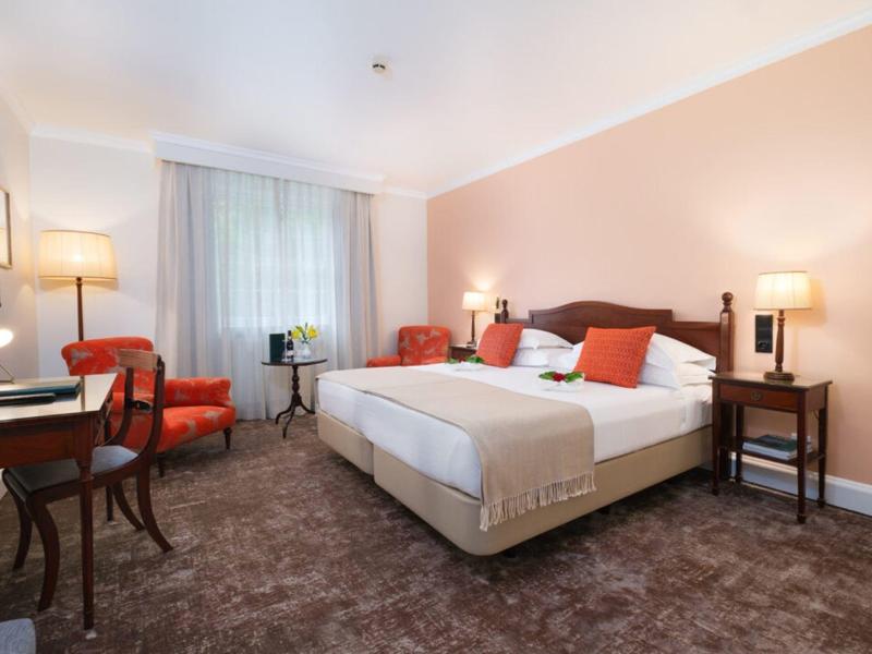 Przytulny pokój hotelowy z dużym łóżkiem podwójnym, fotelami, biurkiem i ciepłym oświetleniem.