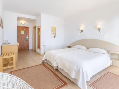 Jasny pokój hotelowy z łóżkiem podwójnym, dwoma stolikami nocnymi i wejściem do korytarza.