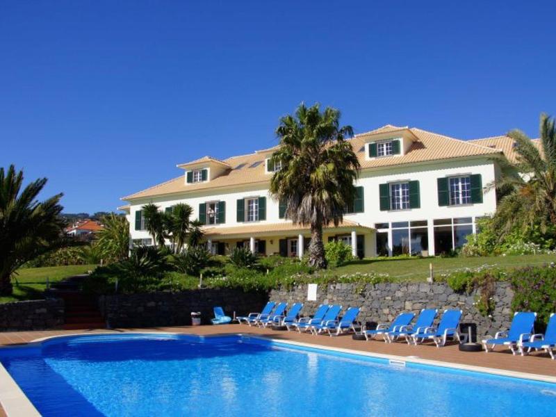 Large hotel with pool in the foreground and clear blue sky.