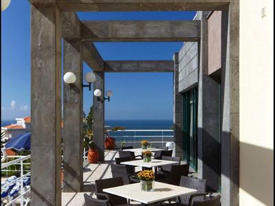 Terrazza con tavoli e sedie, vista sul mare e cielo azzurro.