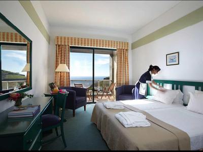 Hotelzimmer mit großem Bett, Balkon mit Meerblick und einer Frau, die das Bett macht.