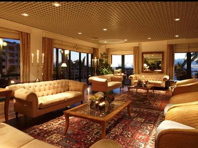 Wohnzimmer mit beigen Sesseln, Sofas, Holztischen, Teppich und warmem Deckenlicht.