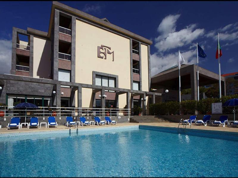 Moderner Hotelkomplex mit großem Swimmingpool, blauen Liegestühlen und sonnigem Himmel.