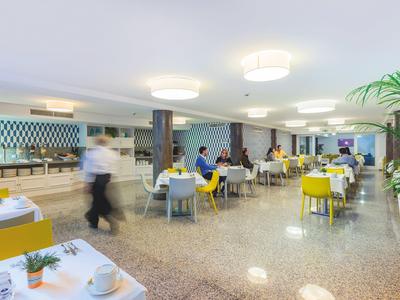 Sala da pranzo dell'hotel luminosa con sedie gialle e grigie e pavimento lucido.